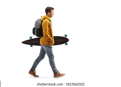 Full length portrait of a male teenage student in a yellow hoodie walking and holding a longboard isolated on white background