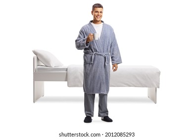 Full Length Portrait Of A Man In A Bathrobe Holding A Cup In Front Of A Bed Isolated On White Background