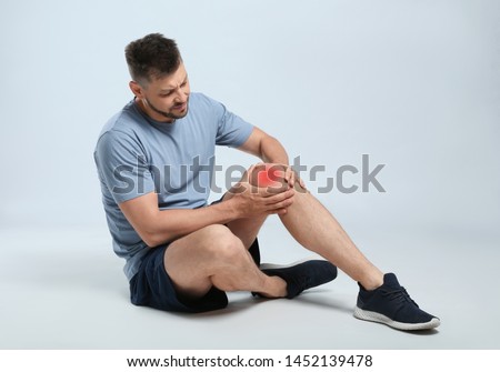 Full length portrait of man with knee problems sitting on grey background