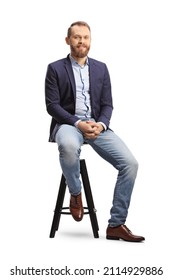 Full length portrait of a man in a suit and jeans sitting on a bar chair isolated on white background
