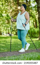 Full Length Portrait Of Mature Black Woman Walking With Poles In Park During Outdoor Workout