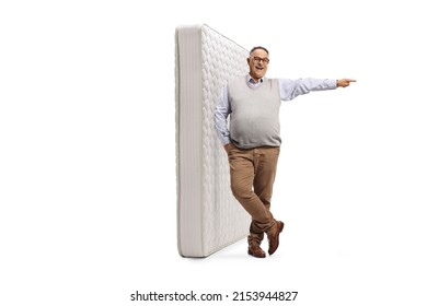 Full Length Portrait Of A Mature Man Leaning On A King Bed Mattress And Pointing To The Side Isolated On White Background