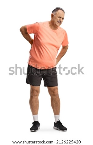 Full length portrait of a mature man in sportswear holding his painful spine isolated on white background