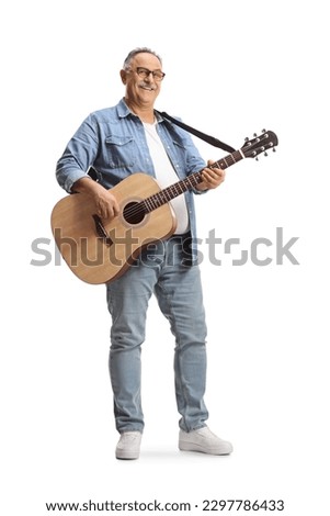 Full length portrait of a mature man standing and playing an acoustic guitar isolated on white background