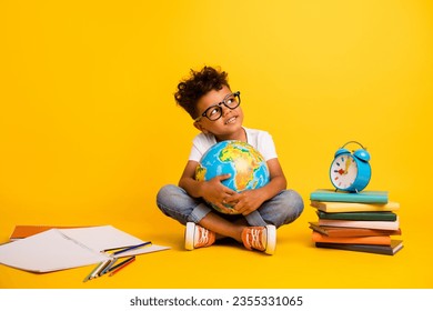 Full length portrait of minded creative little boy sit floor hold world globe look empty space isolated on yellow color background - Powered by Shutterstock