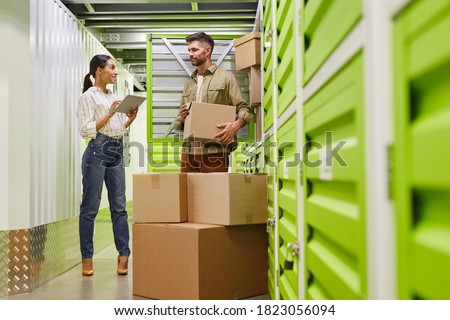 Full length portrait of modern couple using digital tablet while loading boxes into self storage container, copy space