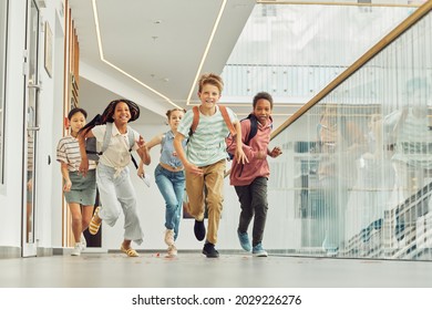 Full Length Portrait Of Multi-ethnic Group Of Schoolkids Running Towards Camera Indoors And Smiling Happily, Copy Space