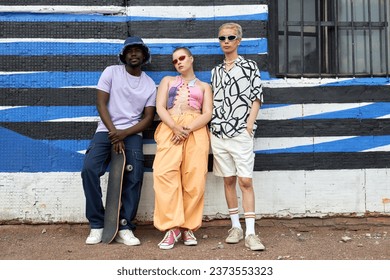 Full length portrait of multiethnic group of young people wearing trendy outfits posing against wall in urban setting, copy space - Powered by Shutterstock