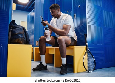 Full length portrait of muscular black sportsman using smartphone in locker room with tennis racket in foreground, copy space - Powered by Shutterstock