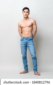 Full length portrait of muscular handsome shirtless Asian man standing and posing in light gray studio isolated background
