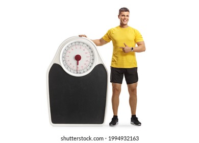 Full length portrait of a muscular man in sportswear leaning on a big scale and pointing isolated on white background - Powered by Shutterstock