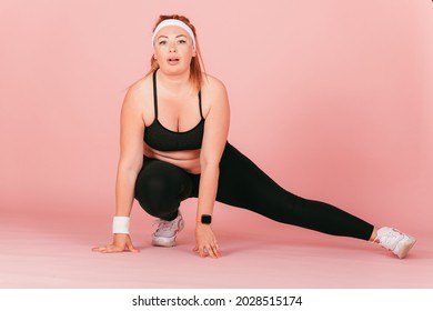 Full Length Portrait Of Plump Woman Doing Physical Exercise, Stretching Her Legs In Squat, Pink Background.