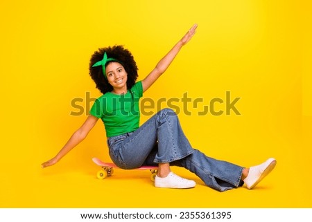 Full length portrait of positive overjoyed person sit skateboard have good mood arms wings isolated on yellow color background