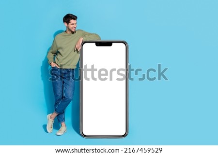 Full length portrait of positive person look empty space huge phone screen isolated on blue color background