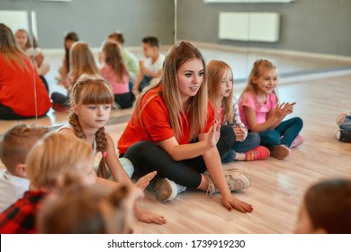 Full length portrait of a postive young dance teacher talking to group of little happy girls and boys sitting on the floor in the dance studio. Relationship between teacher and kids - Powered by Shutterstock