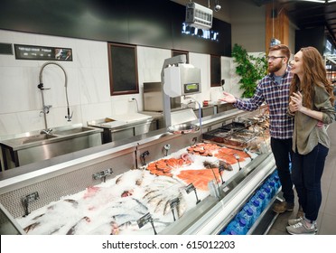 Full length portrait of a pretty  couple choosing fish in supermarket. Side view