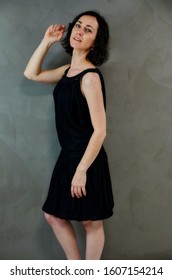 Full Length Portrait Of A Pretty Emotional Brunette Woman In Black Dress On Alternative Gray Background In Vintage Interior. Standing Right In Front Of The Camera.