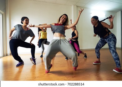 Full length portrait of pretty hip-hop dancer posing for photography with wide smile while standing on tiptoes, her colleagues dancing around her - Shutterstock ID 702288514