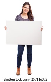 Full length portrait of a pretty Hispanic young woman holding a big white sign and smiling
