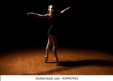 Full length portrait of a pretty Hispanic ballet dancer tip toeing in a dark stage and a spotlight - Powered by Shutterstock