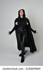 Full length portrait of pretty red haired female model wearing black futuristic scifi leather costume with black flowing cloaked cape. Dynamic standing poses with gestural hands, facing backwards away