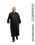 Full length portrait of a priest walking towards camera and holding a bible isolated on white background