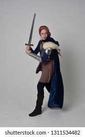 full length portrait of a  red haired girl wearing medieval warrior costume and steel armour, standing pose on grey studio background.
