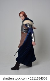 full length portrait of a  red haired girl wearing medieval warrior costume and steel armour, standing pose on grey studio background.
