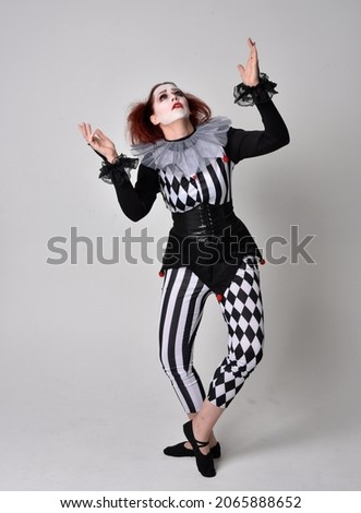 Full length  portrait of red haired  girl wearing a black and white clown jester costume, theatrical circus character.  Standing pose  isolated on  studio background.