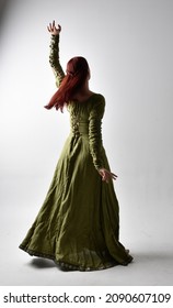 Full length portrait of red head girl wearing  green Celtic medieval gown. Standing  pose with elegant pose, facing away from the camera.  isolated on  studio background 