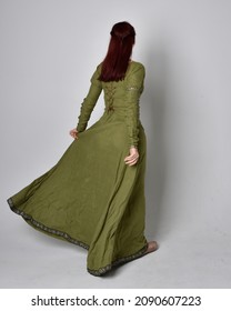 Full length portrait of red head girl wearing  green Celtic medieval gown. Standing  pose with elegant pose, facing away from the camera.  isolated on  studio background 