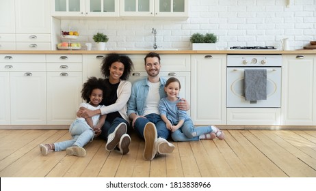 Full length portrait relaxed happy multiracial couple with cute kids sitting on warm wooden floor in modern kitchen. Smiling mixed race family homeowners enjoying peaceful stress free weekend time. - Shutterstock ID 1813838966