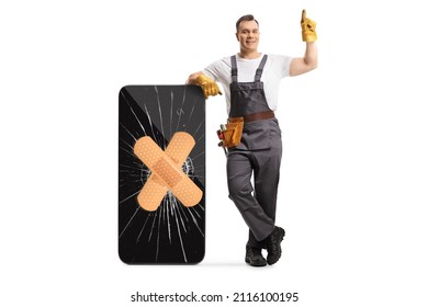 Full length portrait of a repairman leaning on a broken smartphone with bandage and pointing up isolated on white background