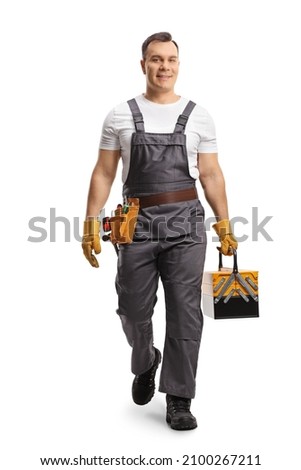 Full length portrait of a repairman in a uniform carrying a tool box and walking towards camera isolated on white background