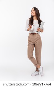 Full length portrait of a satisfied asian businesswoman carrying laptop computer and cup of coffee to go while standing isolated over white background