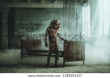 A full length portrait of a scary girl standing near a bed. Halloween. Horror film.