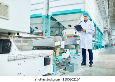 Full length portrait of senior factory worker  holding clipboard standing in clean production workshop, copy space - Shutterstock ID 1100202164