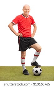 Full Length Portrait Of A Senior Man In A Red Jersey Stepping Over A Football On A Field And Looking At The Camera Isolated On White Background