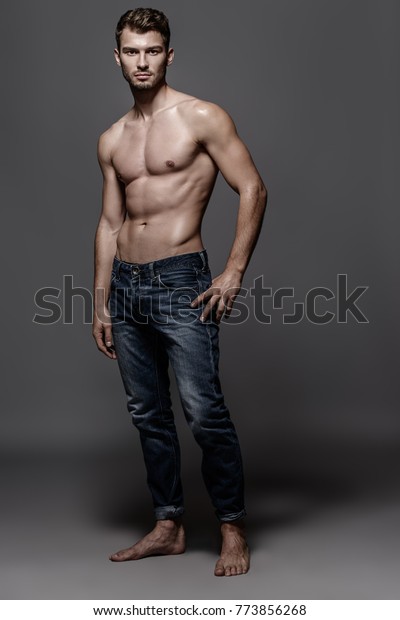 スタジオでポーズを取る ジーンズを着たセクシーな若い男性の全身像 グレイの背景 男性の健康 美容 ジーンズのファッション の写真素材 今すぐ編集 773856268