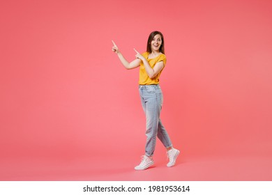 Full length portrait side view of amazed excited young brunette woman 20s in yellow casual t-shirt pointing index fingers aside up on mock up copy space isolated on pink color wall background studio