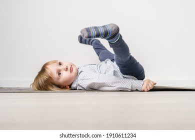 Full length portrait of small caucasian boy laying on the yoga mat on the floor with legs in the air - leisure activity growing up and childhood concept with copy space