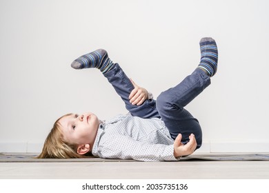 Full length portrait of small caucasian boy laying on the yoga mat on the floor with legs in the air - leisure activity growing up and childhood concept with copy space