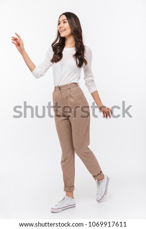 Full length portrait of a smiling asian businesswoman walking and pointing finger away isolated over white background