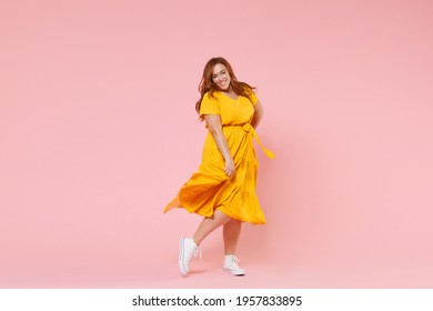 Full length portrait of smiling beautiful charming young redhead plus size body positive female woman girl 20s in yellow dress posing looking camera isolated on pastel pink color background studio - Shutterstock ID 1957833895