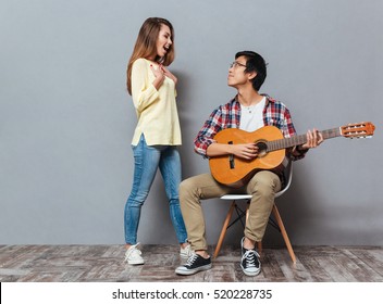 Full length portrait of a smiling happy interracial couple playing guitar isolated on the gray background - Powered by Shutterstock