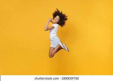 Full length portrait of smiling little african american kid girl 12-13 years old in white t-shirt isolated on yellow wall background studio portrait. Childhood lifestyle concept. Jumping, having fun