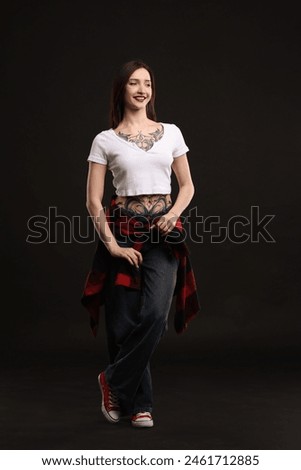 Full length portrait of smiling tattooed woman on black background