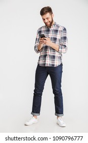 Full Length Portrait Of A Smiling Young Man Using Mobile Phone Isolated Over White Background