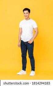Full length portrait of smiling young handsome Asian man standing with one hand in pocket isolated on yellow studio background