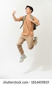 Full length portrait of a smiling young man taking a selfie while jumping isolated over white background